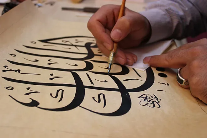 Close-up van een hand die met een rietpen grote Arabische letters schrijft