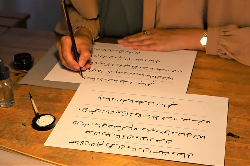 Handen die met een rietpen regels Arabisch schrift oefenen op wit papier