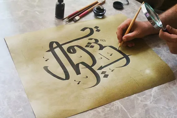 Een kalligraaf schrijft met een rietpen op goudkleurig papier
